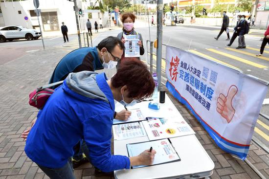People sign at a street counter in support of improving the electoral system of the Hong Kong Special Administrative Region (HKSAR) and implementing the principle of 