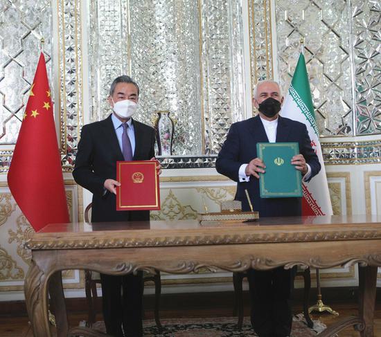 Visiting Chinese State Councilor and Foreign Minister Wang Yi (L) and Iranian Foreign Minister Mohammad Javad Zarif pose for photos with agreements on the China-Iran comprehensive cooperation plan in Tehran, Iran, on March 27, 2021. (Photo by Ahmad Halabisaz/Xinhua)