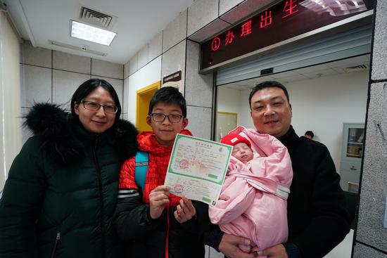 A man holding his newly-born second child poses for a group photo with his wife and his first son, who shows the medical certificate of birth of his little sister. (Xinhua/Ji Chunpeng)