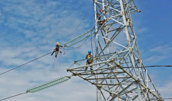 State Grid employees undertake maintenance work on a tower in Taizhou, Zhejiang province, in April. (WANG HUABIN/FOR CHINA DAILY)
