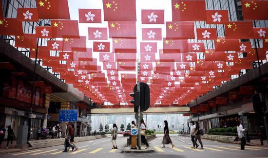 People walk past China's national flags and the flags of the Hong Kong Special Administrative Region for the celebration of 24th anniversary of Hong Kong's return to the motherland at Tsim Sha Tsui East in Hong Kong on June 29, 2021. (chinadaily.com.cn/Edmond Tang)