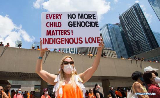 A woman holds a placard during a rally in Toronto, Canada, on July 1, 2021. Hundreds of people gathered here on Thursday to pay tribute to indigenous children whose bodies were found in mass graves near former indigenous residential schools in Canada. (Photo by Zou Zheng/Xinhua)