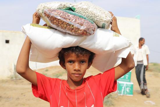 Photo taken on Feb. 14, 2021 shows a boy carrying the food donated by a charity group in Hajjah Province, north Yemen. (Photo by Al-Wafi Mohammed/Xinhua)