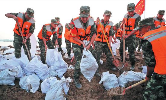 Soldiers from the People's Armed Police Force fortify a dam on Saturday after a local river overflowed due to recent downpours in Xinxiang, Henan province. (WANG JING/CHINA DAILY)