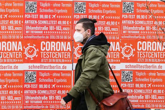 A pedestrian wearing a face mask walks past posters of a COVID-19 test site in Berlin, capital of Germany, April 16, 2021. (Photo by Stefan Zeitz/Xinhua)