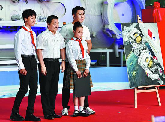 Yang Liwei (second left), China's first astronaut in outer space, is given a painting of a spacewalk by students attending the opening ceremony of an exhibition on the Chinese space station in Beijing on Monday. WEI XIAOHAO/CHINA DAILY