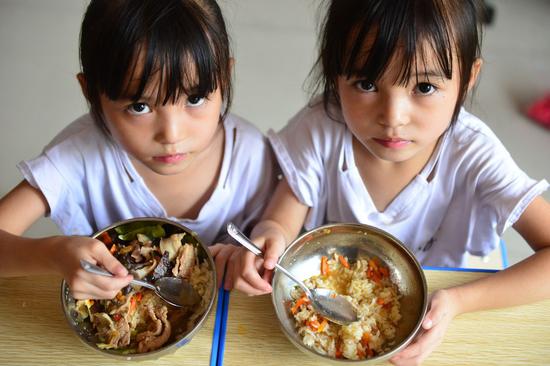 File photo taken in 2017 shows twin girls Liu Yuting (R) and Liu Yuyao take free lunch at the No. 4 Primary School in southwest China's Guizhou Province. Free lunch project has improved diets of rural students in Guizhou since 2012. The nutritious lunches helped address malnutrition among students in remote and poor areas. (Xinhua/Yang Wenbin)