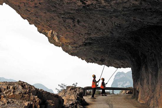 Huang Qifu (left) and his colleague clean loose rocks along the cliff road leading to Shibanhe village in Bijie city, Guizhou province in 2019. (Photo: China Daily/Han Xianpu)