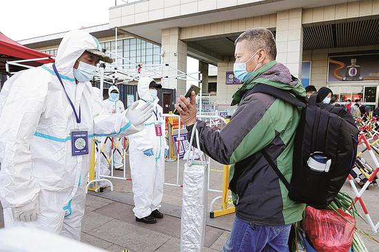 An epidemic control worker checks a passenger's health code at a railway station exit in Yantai, Shandong province, on Monday. The latest COVID-19 outbreak has affected 16 provincial-level regions nationwide. (TANG KE/FOR CHINA DAILY)