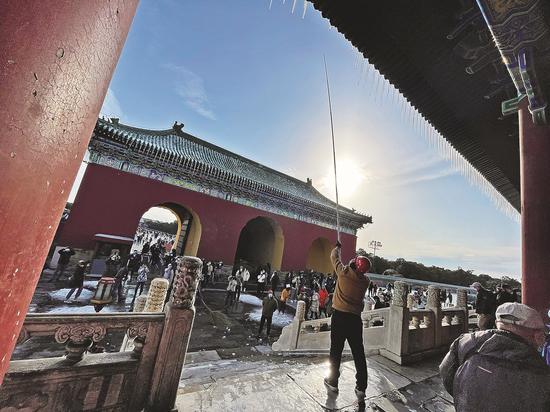 A worker knocks icicles off the eaves of a building in Beijing's Temple of Heaven Park on Sunday after snow and ice accumulated overnight. (Photo: China Daily/Du Lianyi)