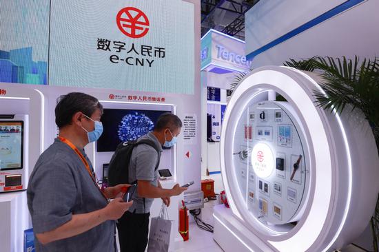 Visitors view information at a booth promoting the e-CNY during an expo in Beijing. [Photo by Chen Xiaogen/For China Daily]