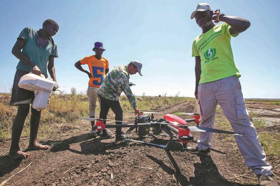 A Chinese agricultural expert (second from right) shows workers how to use a drone to spray herbicides over a rice farm in Mozambique. Thanks to China's technical support, yields at the Chinese-backed farm have increased significantly. (Photo: Xinhua/Lin Shanchuan)