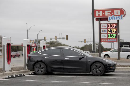  A Tesla electric car charges as gas prices are advertised in San Antonio, Texas, the United States on Feb. 24, 2022. (Photo by Nick Wagner/Xinhua)