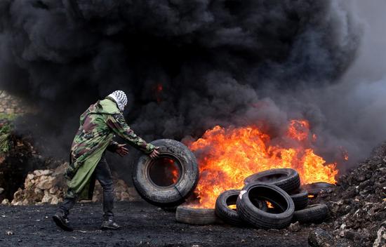 A Palestinian protester burns tires during clashes following a protest against the expanding of Jewish settlements in Kufr Qadoom village near the West Bank city of Nablus, March 18, 2022. (Photo by Nidal Eshtayeh/Xinhua)