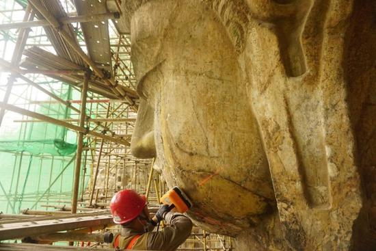 Undated file photo shows an archaeologist examining the face of a Buddha statue at the Fengxiansi Cave of Longmen Grottoes in central China's Henan Province. (Longmen Grottoes Research Institute/Handout via Xinhua)
