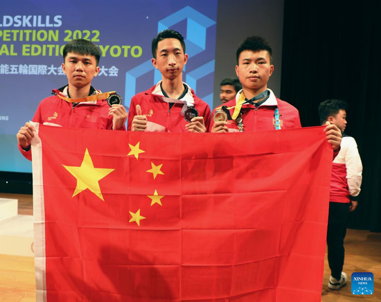 Chinese competitors Chen Zhiyong, Zhang Honghao and Li Xiaosong (from L to R) pose for a photo with the Chinese national flag and their medals during the awarding ceremony of the WorldSkills Competition 2022 Special Edition in Kyoto, Japan, Oct. 19, 2022. (Photo/Xinhua)