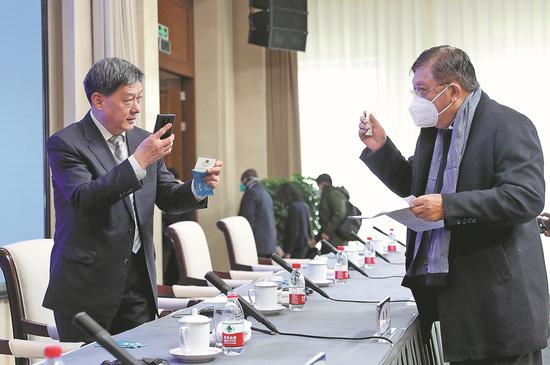 Jean-Louis Robinson (right), ambassador of Madagascar to China, exchanges business cards with Liu Qingquan, president of the Beijing Hospital of Traditional Chinese Medicine, after a policy briefing in Beijing on Friday. (Photo by Zou Hong/China Daily)