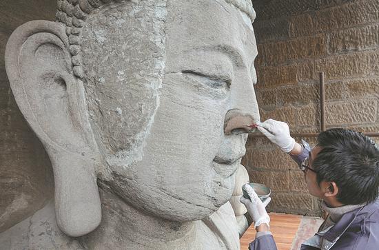 Repairs are made to a 14th century sculpture in a grotto near the Yangtze River in Chongqing. (Photo/Xinhua)
