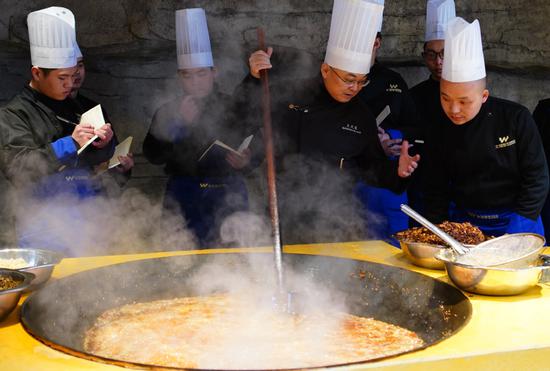 Hotpot expert Wang Wenjun (center right) teaches students how to fry hotpot sauce at Chongqing Wen Zhi Su Hotpot Catering School in Chongqing on March 9. (Photo/China Daily)