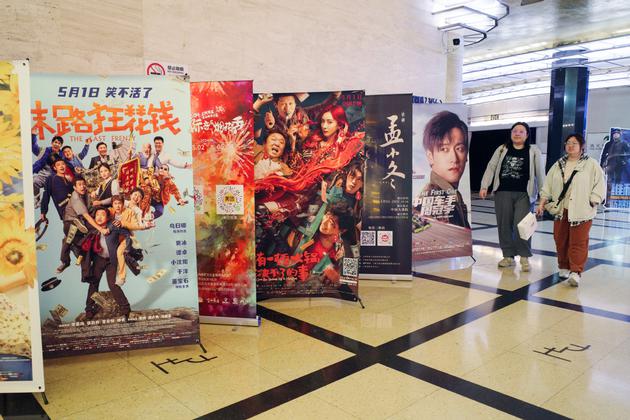 Cinemagoers walk past posters for films that are screening at a movie theater in Shanghai on Tuesday. CHINA DAILY