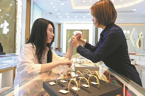 A shopper tries on a gold bracelet at a jewelry store in Chongqing. （SUN KAIFANG/FOR CHINA DAILY）