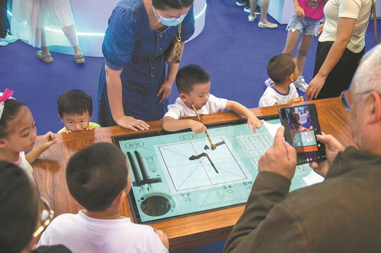 A child experiences writing with a Chinese calligraphy brush on a digital screen at the 14th China International Digital Publishing Expo in Hainan province on Saturday. (Photo provided to China Daily)