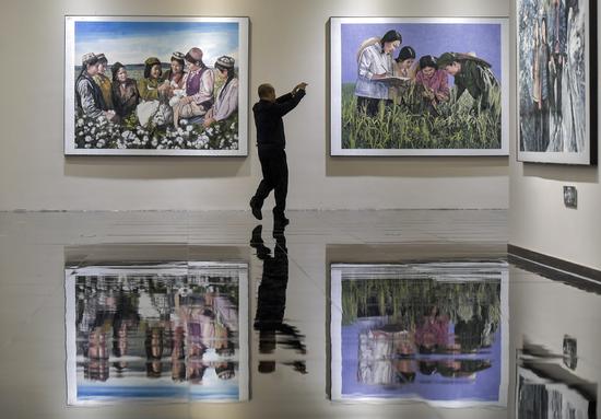 A visitor takes a photo of a painting at an art exhibition celebrating the 70th anniversary of the founding of the Xinjiang Production and Construction Corps in Urumqi, capital of the Xinjiang Uygur autonomous region, on Sept 26. The themed exhibition runs through Oct 15. (LIU XIN/CHINA NEWS SERVICE)