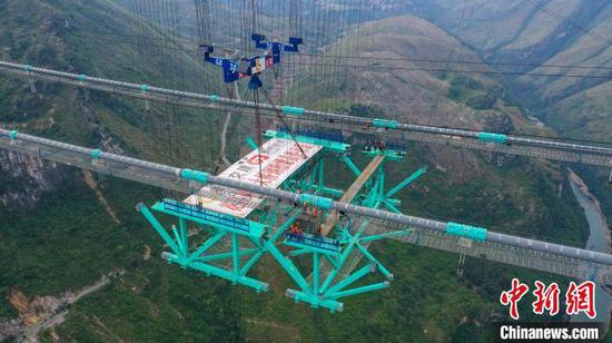 An aerial drone photo taken on Nov. 4, 2024 shows the Huajiang Grand Canyon Bridge's first steel truss girder, weighing about 215 tonnes, being hoisted to its designated position for installation in southwest China's Guizhou Province, Nov. 4, 2024. (Photo/China News Service)