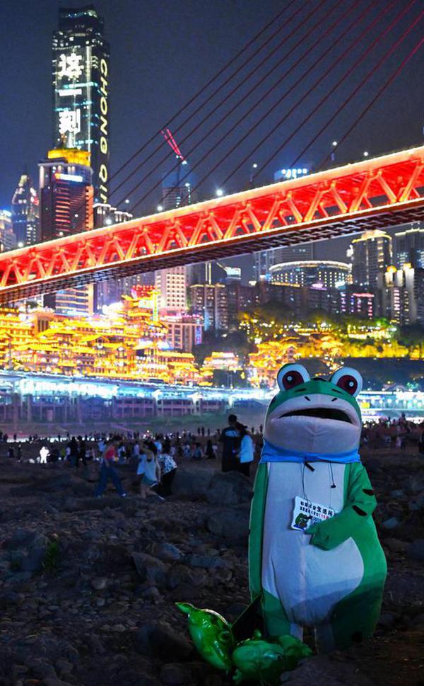 Following urban renewal, a riverside park under a bridge in Jiangbei district of Chongqing has become a popular spot for tourists and residents to enjoy the night view. A toy vendor selling popular frog toys poses for a photo. (Photo by Li Ye/For chinadaily.com.cn)