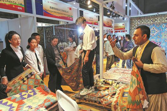 An Afghan exhibitor (right) introduces carpets to customers at the Lhasa Import Expo at the Xizang Exhibition Center in Lhasa, Xizang autonomous region, on Aug 4. The event attracted more than 200 companies and over 600 foreign merchants from 31 countries and regions. (JIANG FEIBO/CHINA NEWS SERVICE)