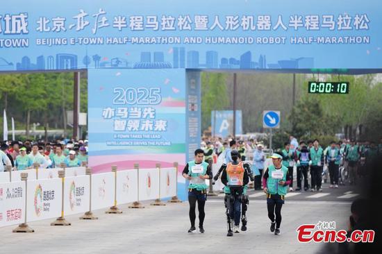 Robotic participant "Tiangong Ultra" competes as engineers run alongside during the Beijing E-Town half-marathon and humanoid robots half-marathon in the Beijing Economic-Technological Development Area, April 19, 2025. (Photo: China News Service/Jia Tianyong)