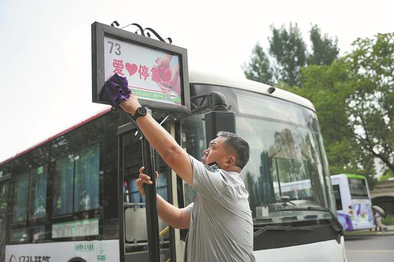 Mei cleans the sign of "compassionate bus stop" in Xiangyang. (Photo/China Daily)