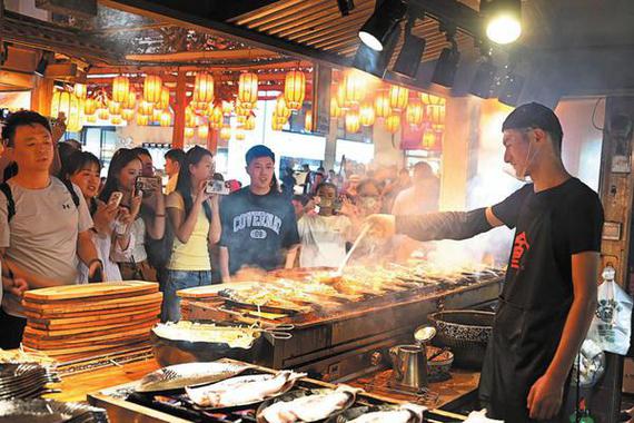 Tourists watch a man cooking local specialties at a night market in Dunhuang, Gansu province, on Aug 16. (ZHANG XIAOLIANG/FOR CHINA DAILY)