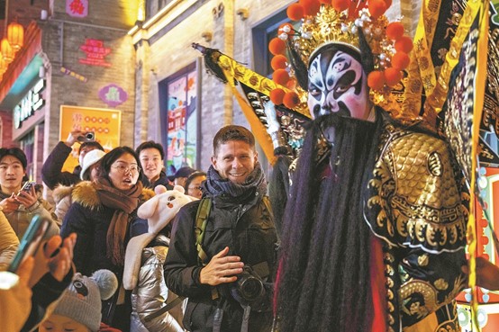 A foreign tourist poses with a performer wearing a Peking Opera costume, while visiting the bustling Qianmen commercial area in Beijing on Sunday. (Photo/China Daily)