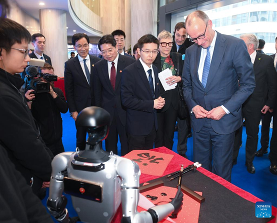 German Chancellor Friedrich Merz, who is on an official visit to China, watches a humanoid robot of Unitree Robotics writing the Chinese character "Fu", meaning "good fortune", in Hangzhou, east China's Zhejiang Province, Feb. 26, 2026. (Xinhua/Weng Xinyang)