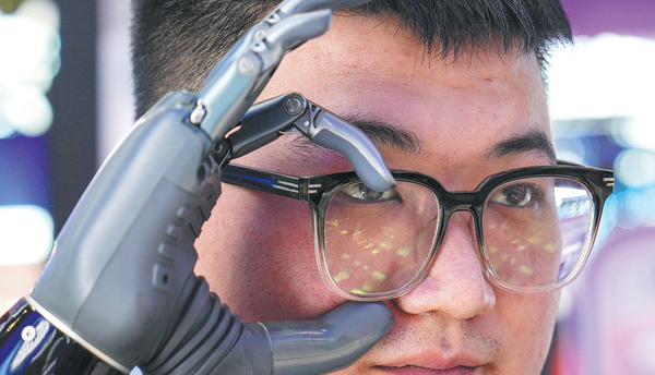 A staff member with a disabled right hand from BrainCo takes off glasses with the company's intelligent bionic hand during the third China International Supply Chain Expo in Beijing on July 17. (JU HUANZONG/XINHUA)