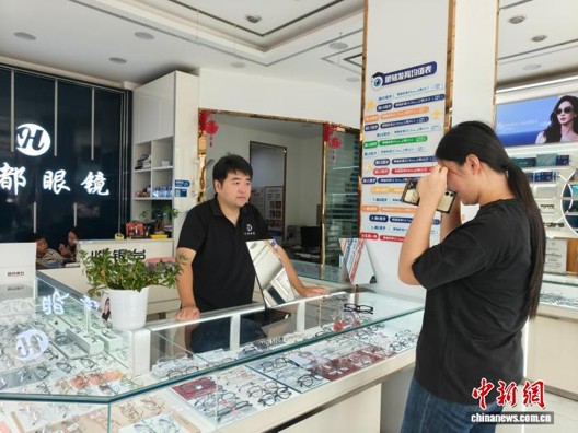 Chen Aijun, an eyeglasses shop owner and AI video creator, introduces products at his store, August 11, 2026. ( Photo: China News Service/ Chen Xuanbin)