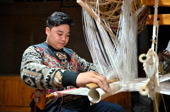 11月23日，广西来宾市忻城县，“90后”壮族男子兰培文正坐在传统竹笼机前织锦。 俞靖 摄
