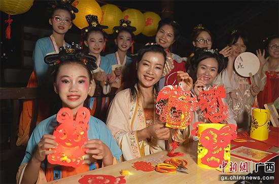 图二:玉林市非物质文化剪纸传承人梁嗣银带领游客动手制作花灯。宁诗琪 摄