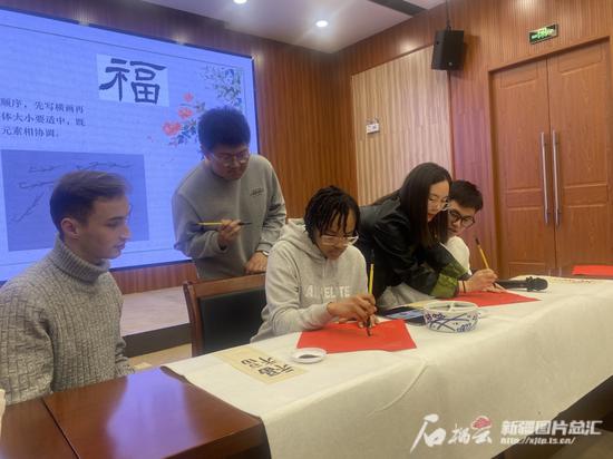 1月12日,代表团成员和新疆大学学生一起学习书法,写“福”字。王新 摄