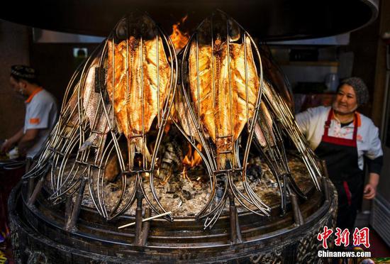 11月1日，位于乌鲁木齐市二道桥的新疆国际大巴扎美食街正式开启冬季运营模式。在未来长达半年的冬季，经过升级改造后的透明全景暖房“冰屋夜市”，将为游客提供具有新疆特色的就餐环境。夜市中21个美食档口，可加工制作超过170种新疆美食，让游客一站即可吃遍新疆美食。图为“冰屋夜市”中的新疆烤鱼档口。中新社记者 刘新 摄