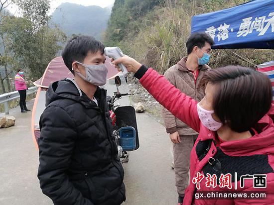 图为九圩镇拉架村女党员唐彩金在监测点值守，为过往人员量体温。