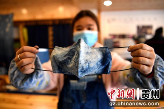 3月18日,在贵州省榕江县卧龙移民安置小区,一移民姑娘在扶贫车间里展示用蓝染侗布制作的口罩。王炳真 摄 3月18日,在贵州省榕江县卧龙移民安置小区,一移民姑娘在扶贫车间里展示用蓝染侗布制作的口罩。王炳真 摄