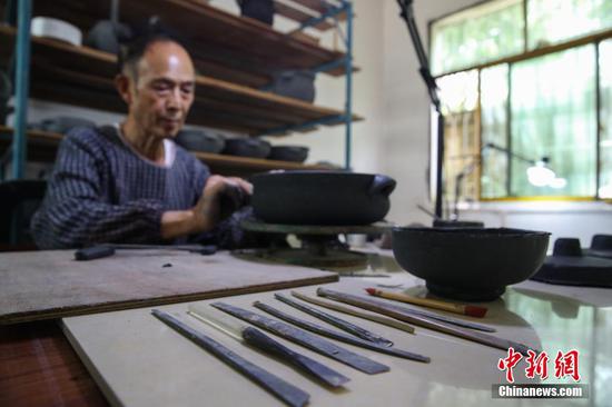“黑砂陶”是无釉陶器的分支，具有悠久的历史。该陶属于高温陶种，成品器具手工制作工序繁多，需要经过采泥、配料、塑形等10多道工序，并通过1300℃高温烧制后才能成形。今年74岁的胡正德是贵州贵阳清镇市犁倭镇黑砂陶制作技艺传承人，他从1988年开始研究黑砂陶制作工艺，并将其进行不断开发和创新，目前已经掌握了10余种黑砂陶器具制作技艺。图为8月5日，胡正德塑形“黑砂陶”器具。 中新社记者 瞿宏伦 摄