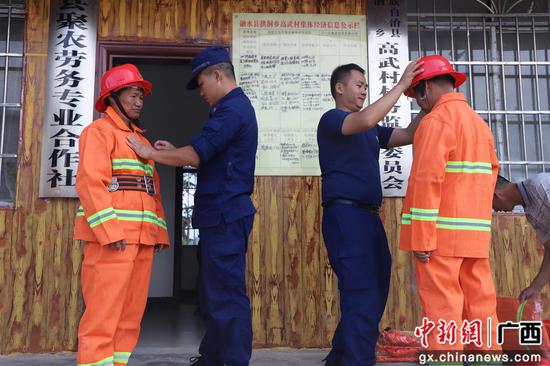 消防员教村义务消防员穿戴消防衣帽。