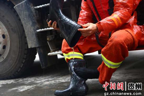 图为清淤结束后,消防指战员坐在消防水罐车器材箱的挡板上,脱下水鞋,泥水倾泻而出。