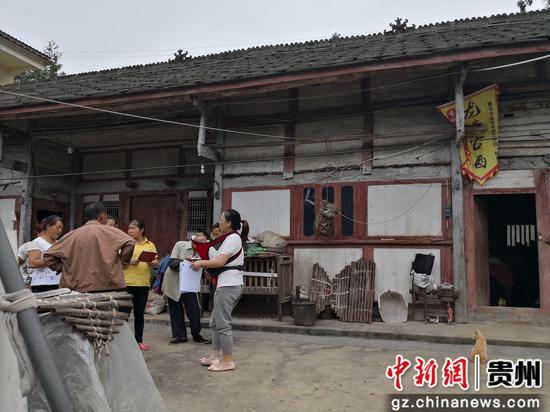 图为姚孝红背着孩子走访。