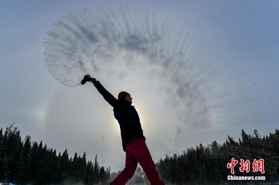 12月23日，新疆阿勒泰地区喀纳斯景区，气温在零下20℃以下，一位游客将杯中热水洒向空中，体验泼水成冰。冬季的喀纳斯景区银装素裹，雪原、冰湖、雾凇相映，如同一幅水墨画卷。 中新社记者 刘新 摄