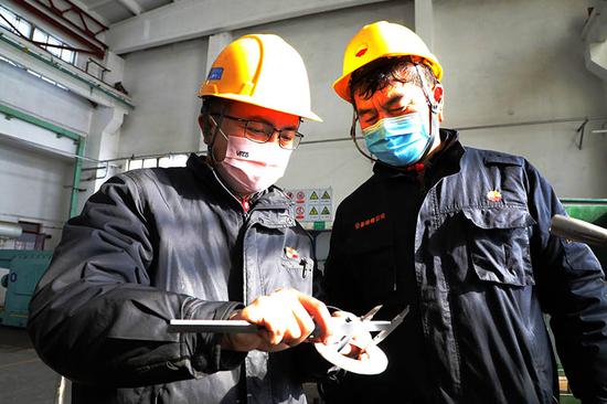 马进（左）和班组员工正在测量设备配件尺寸。李秦 摄