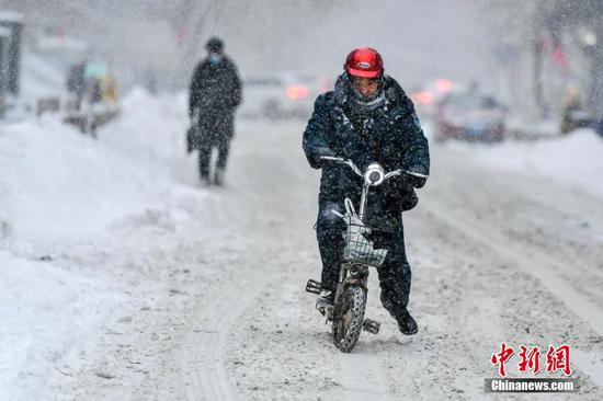 1月23日，新疆乌鲁木齐市迎来一场强降雪天气，骑电动车外出的市民用脚辅助在雪地中骑行。 中新社记者 刘新 摄